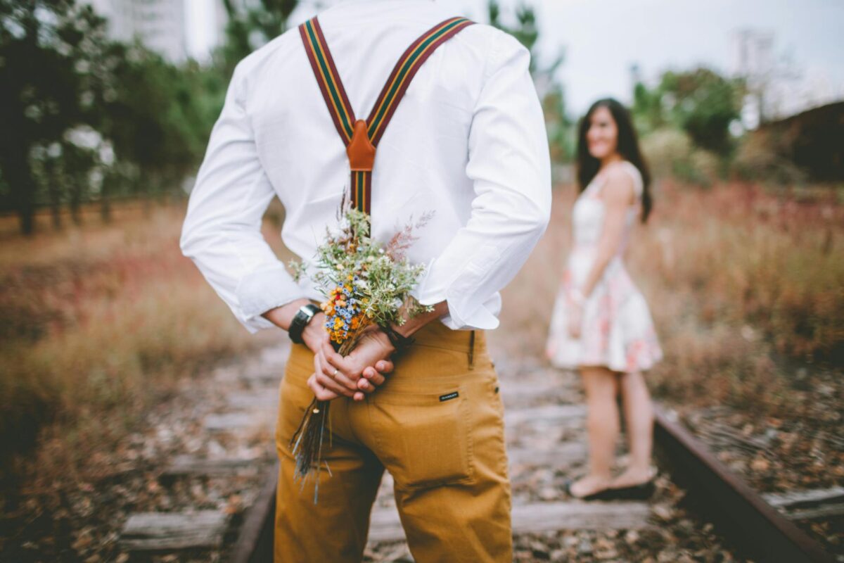 man holding flowers standing beside woman on railroad