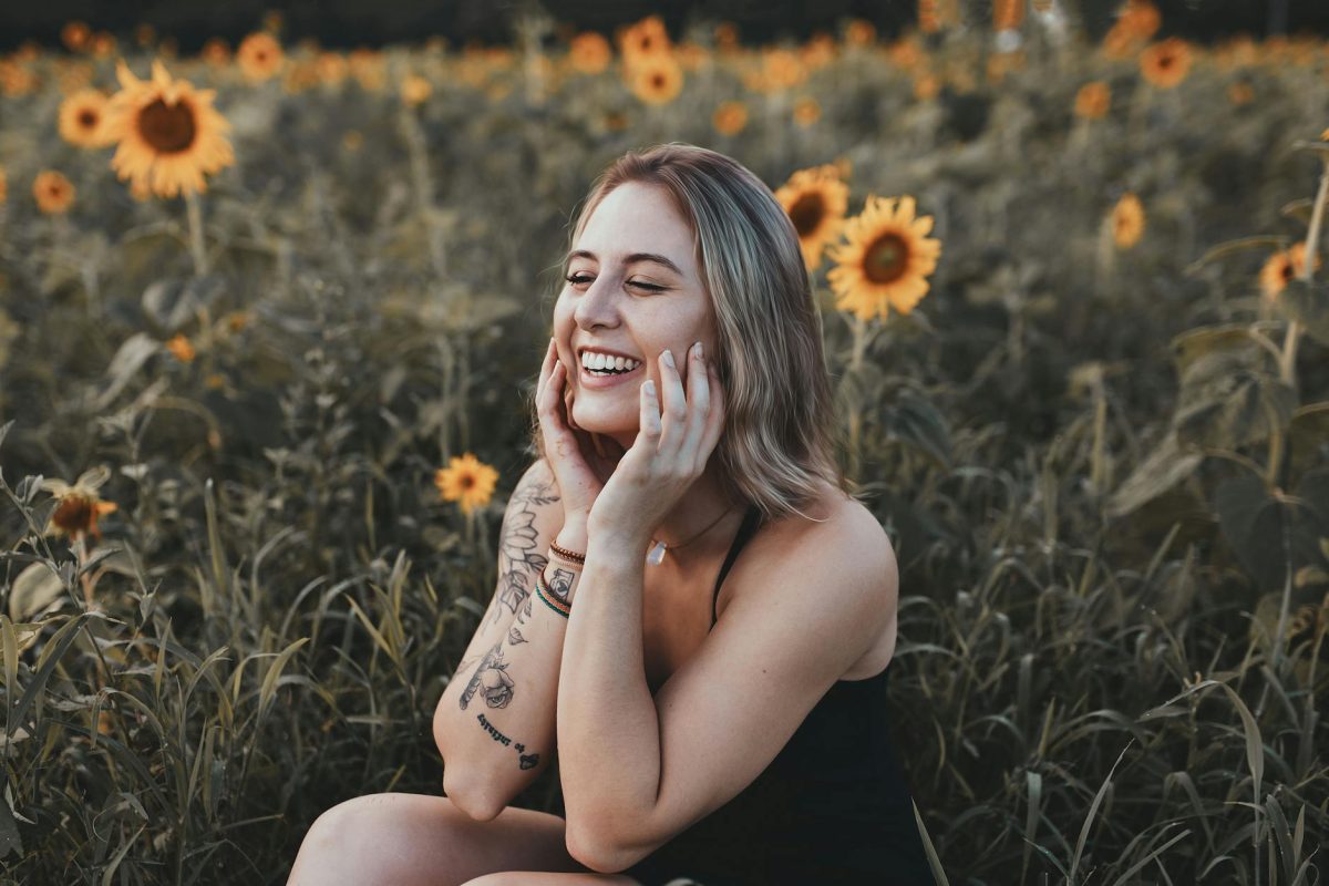 woman in black tank top sitting on yellow flower field laughing